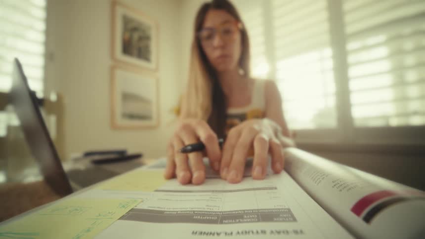 A woman sits at a table and flips through the pages of a textbook titled 75day study planner she then holds a pen and begins writing notes or filling out sections within the planner