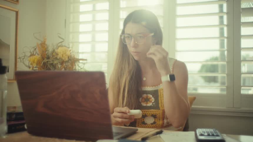 Teenage girl sitting at a desk with a laptop computer putting earbuds into her ears