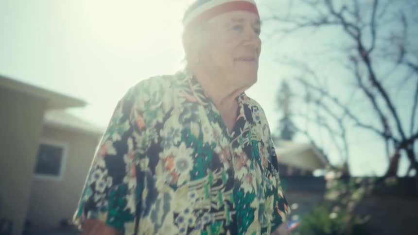 Elderly man smiles and moves his arms as he dances in his front yard