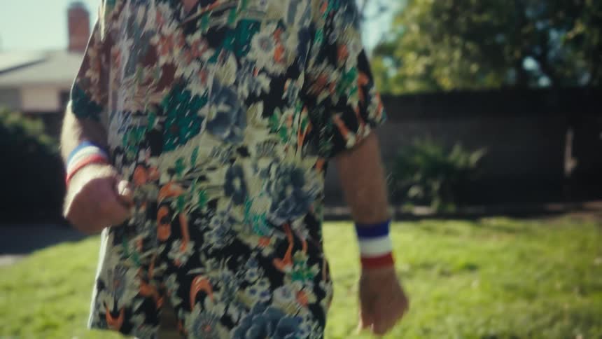Elderly man smiles and moves his arms as he dances in his front yard