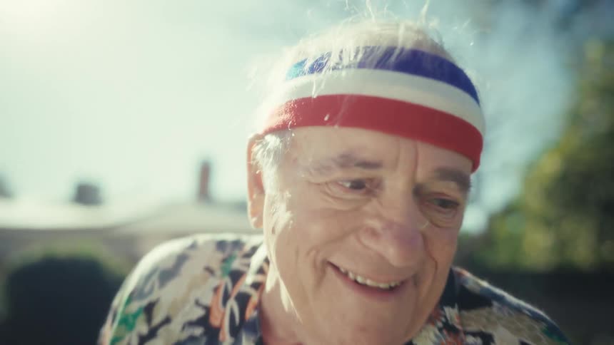 Elderly man wearing a sports headband walks in the backyard under sunlight