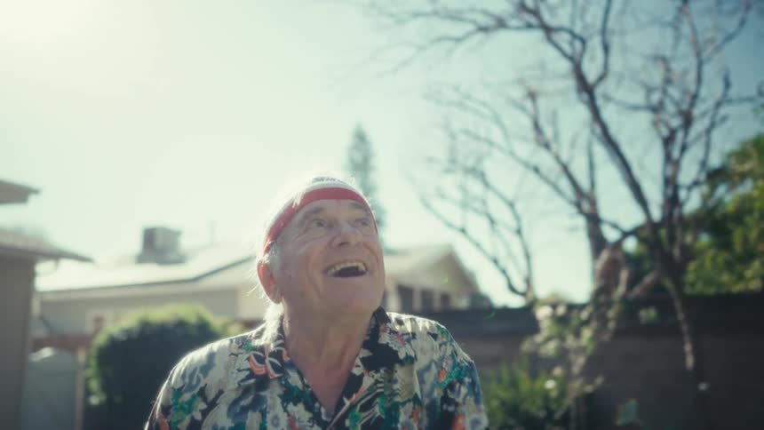 Elderly man wearing a sports headband and colorful wristbands dances on the backyard lawn