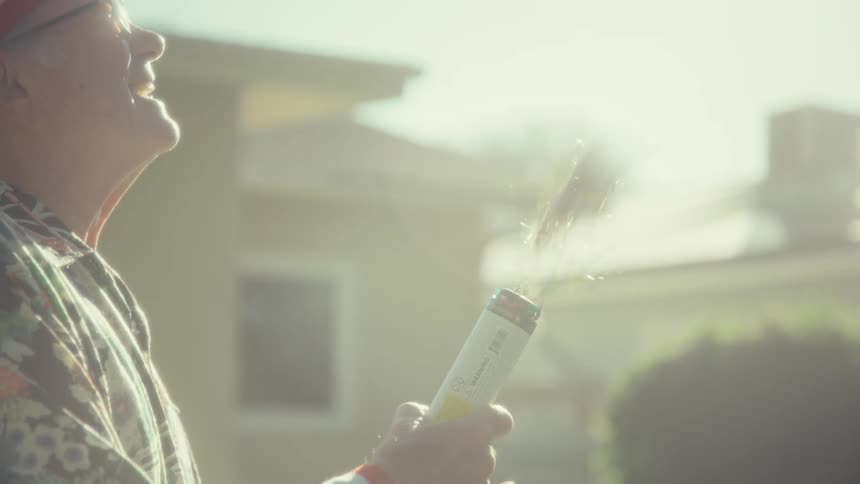 Elderly man holds a can that releases confetti in the backyard under sunlight