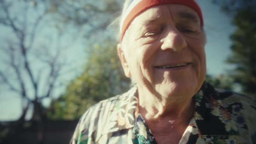 Senior man wearing a headband jogs through a sunny backyard garden