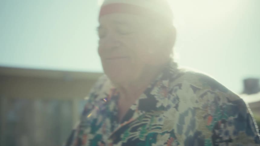 An elderly man doing yoga stretches in his backyard wearing a headband and wristbands enjoying himself