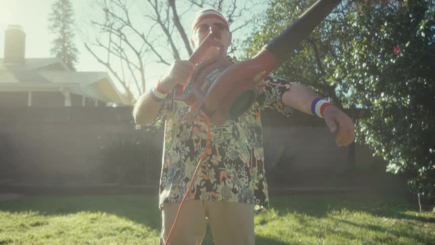 Elderly man wearing a sports headband holds a leaf blower in the backyard under sunlight
