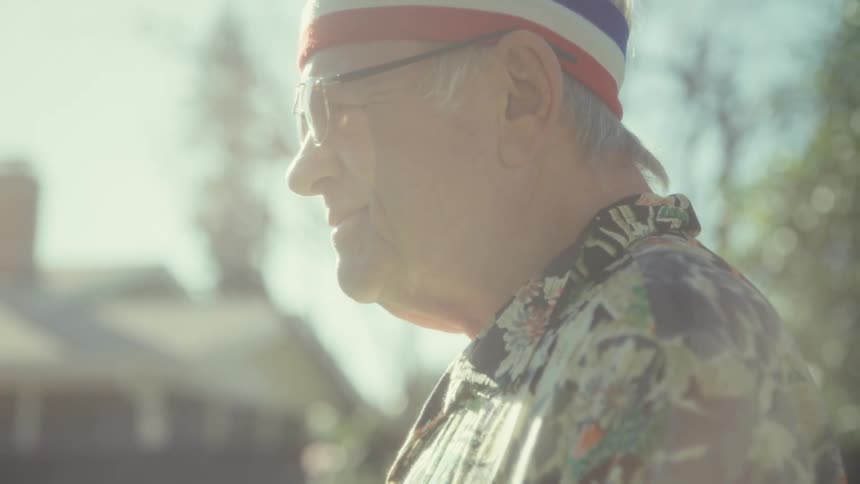 A camera tilts up an elderly man dressed in vintage workout gear