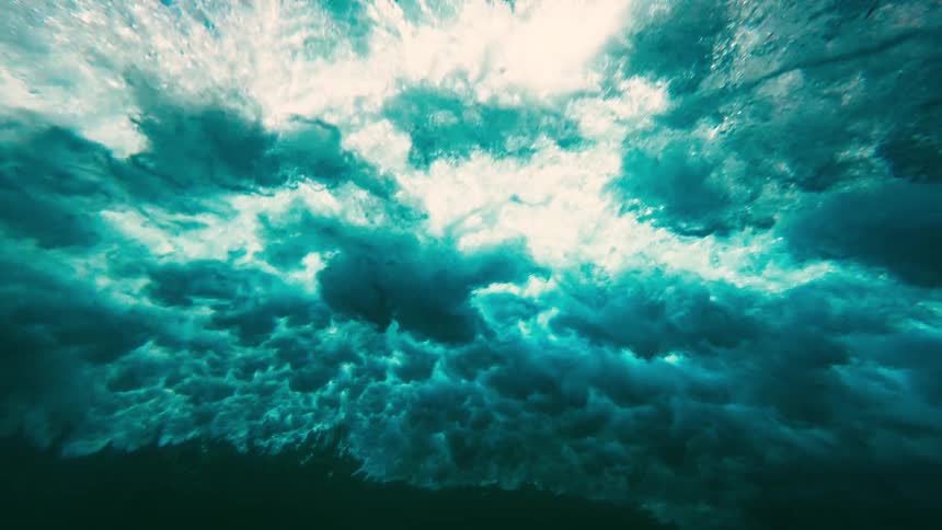Underwater footage captures a crashing wave from below showing the surface churn into white foam and bubbleslight filters through the turbulent water creating a highcontrast view of the oceans raw energy