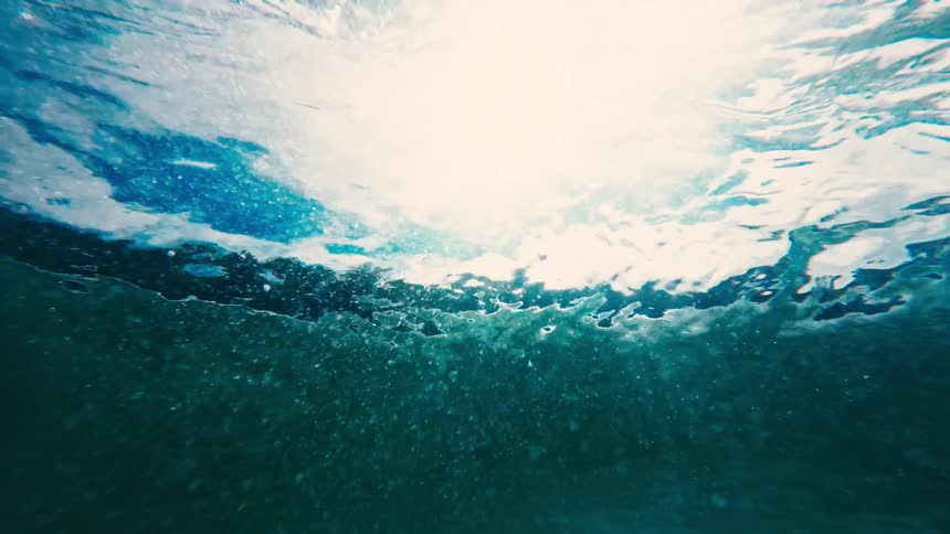 Waves and foam seen from beneath the surface of blue water