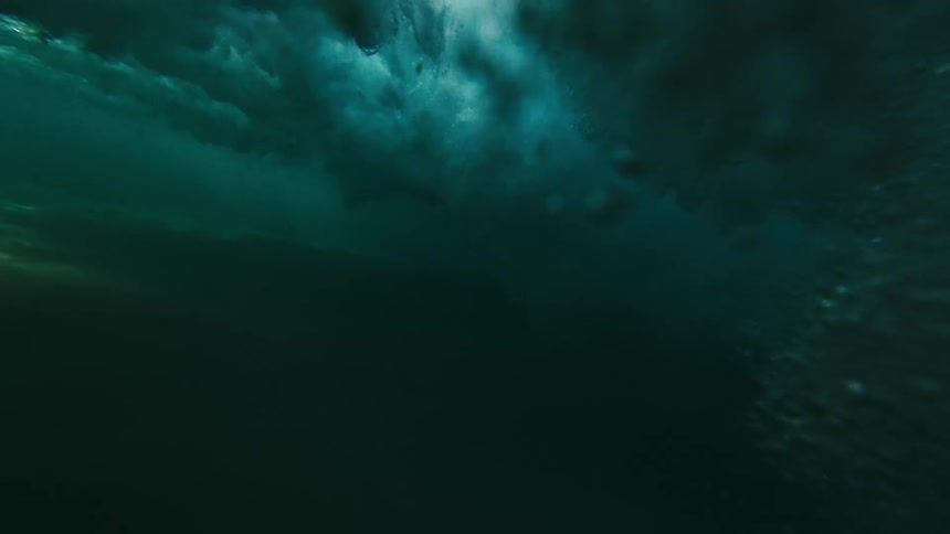 Wave foam moves beneath the surface while light reflects on the sandy bottom