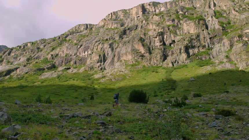 Hiker walking up a green hill towards some mountains