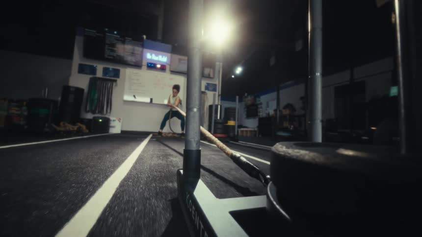 Young woman pulls a rope with weights as she exercises in the gym