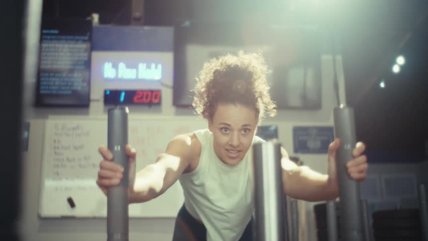 Woman exercises on gym equipment holding vertical bars