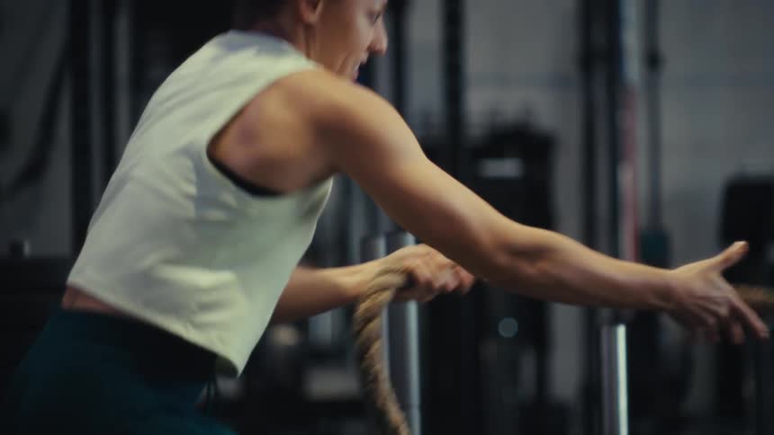 Woman performs a rope exercise in a gym seen from the side