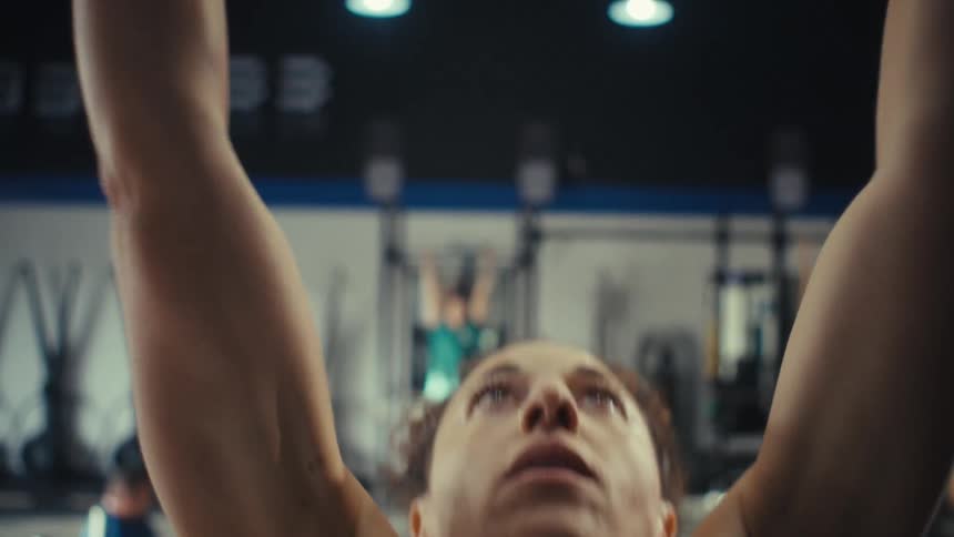 A woman with curly hair takes a deep breath to focus before reaching up to grab a pullup bar she successfully completes a repetition pulling her chin above the bar before dropping back down to the floor