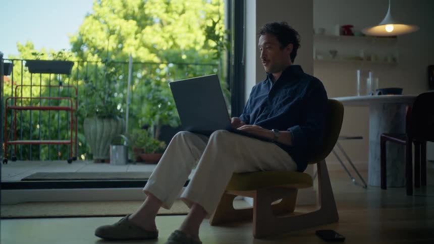 Man sitting in a chair having a conversation on the laptop computer in his lap