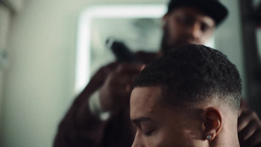 A male barber cutting a mans hair inside his shop at midday