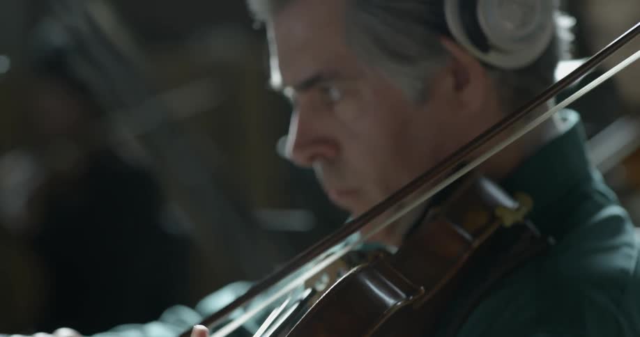 A man wearing headphones plays the violin