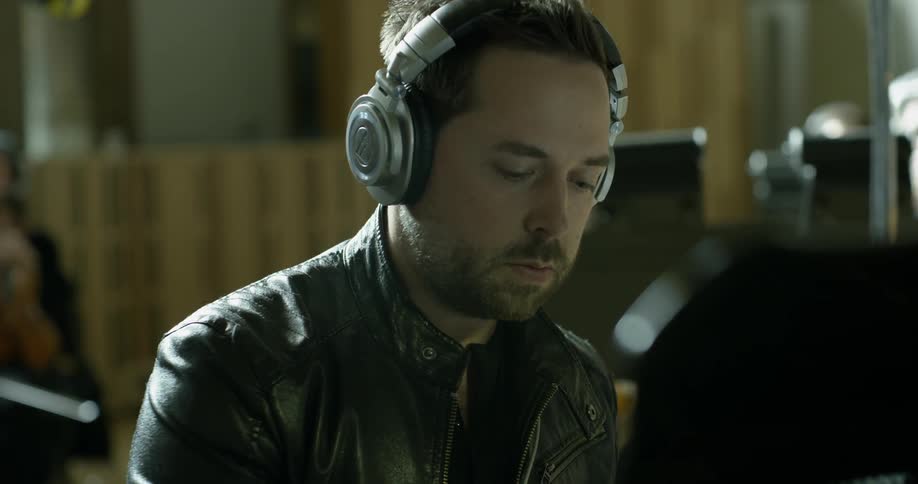 A man in a leather jacket listens on headphones