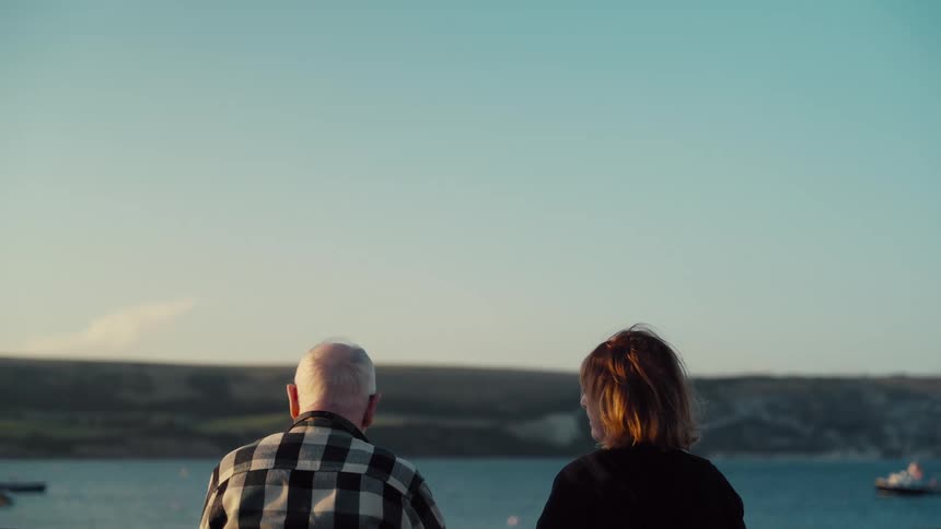 Elderly man sits with a younger woman in an area overlooking the water