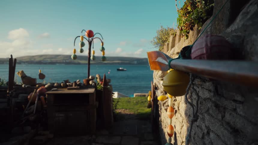 Oar resting against a stone wall with colorful buoys beside a coastal area with the sea in the background