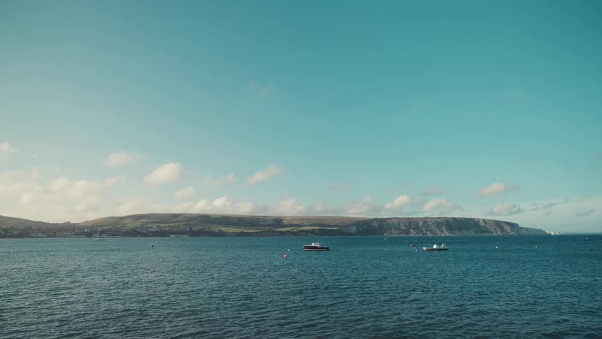 Boats sail on the water off the coast as clouds move across the sky