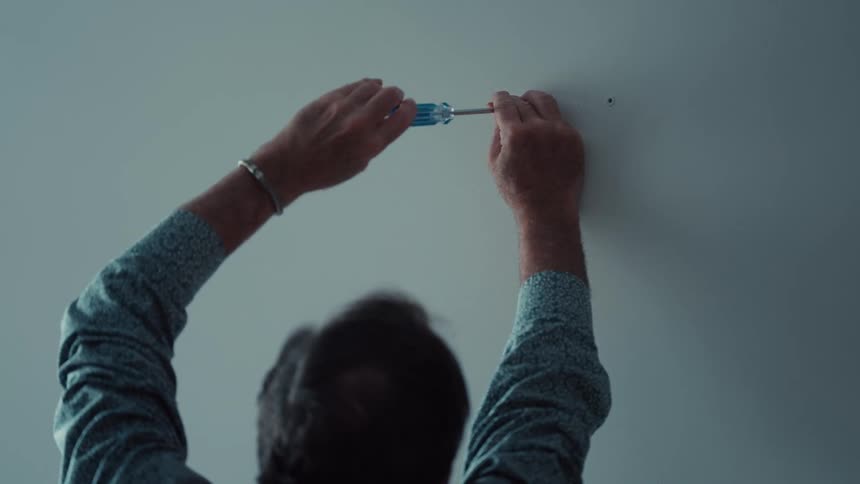 The man is manually screwing a screw into the wall