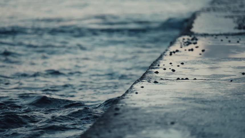 Waves roll past a concrete waterfront in the early evening