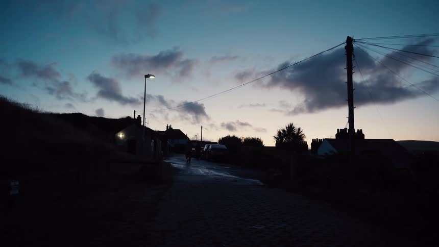 Pedestrians walk on a wet road in a residential neighborhood at night