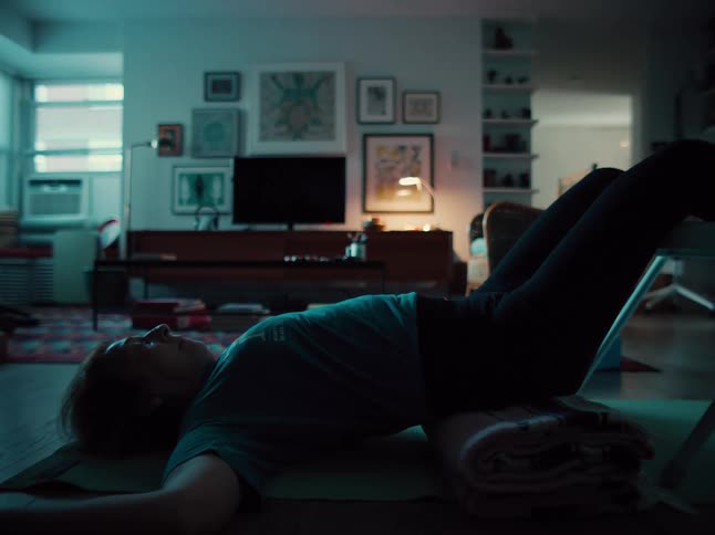 Woman lies on the floor with raised legs and a blanket under her hips at home