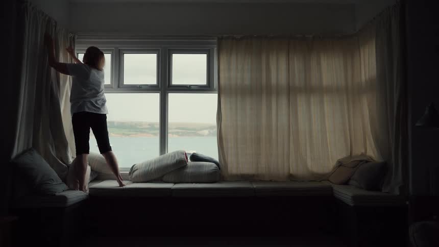 The woman is opening the drapes in her home