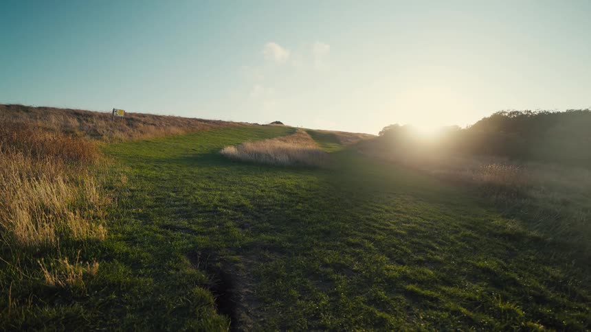 Dirt and grass path leads to a hill illuminated by the low sun on the horizon