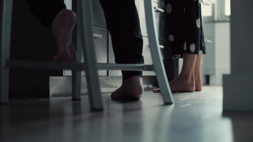 This video shows a lowangle shot focusing on the bare feet of two people standing in a kitchen they shift their weight and move slightly while seemingly engaged in a task at the counter