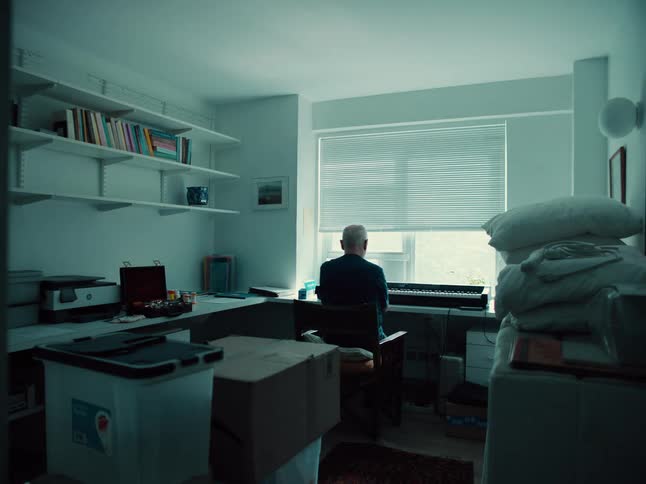 White haired man plays an electric keyboard near the window at home