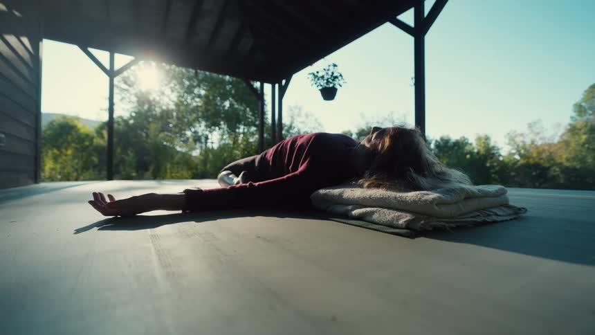 Woman lying on blankets on a covered porch with sunlight in the background