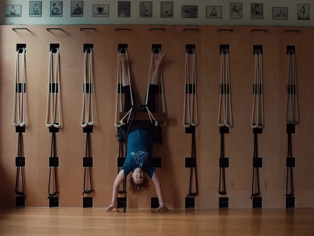 The woman hangs from ropes in the gym upside down