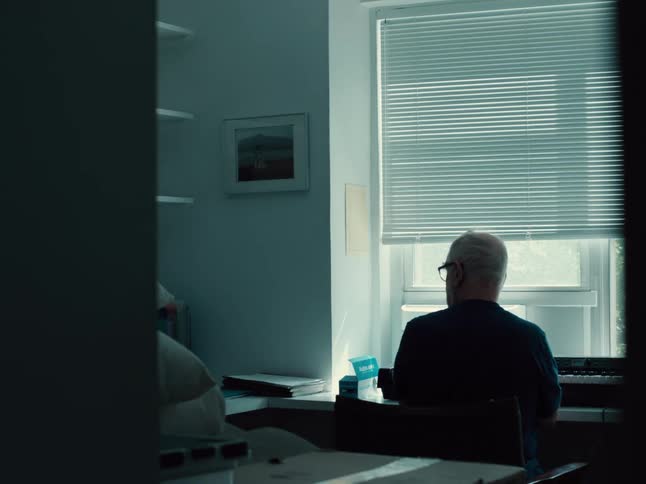 Elderly man plays an electric keyboard while sitting near the window during the daytime