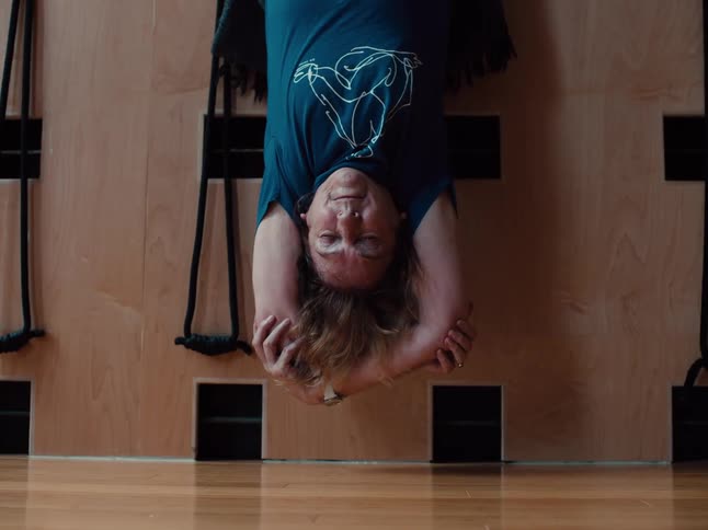 Person performs an inverted stretch against a wall in an indoor space with a wooden floor