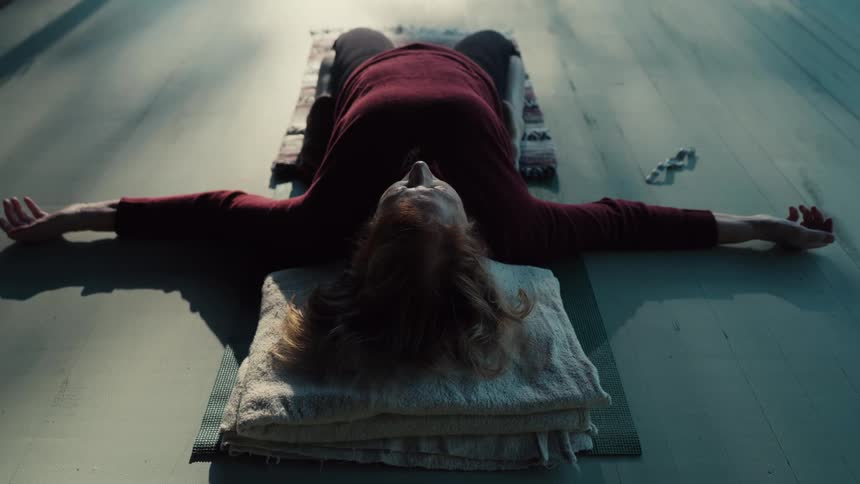 Person lying on their back with arms outstretched on cushions in an indoor space lit by natural light