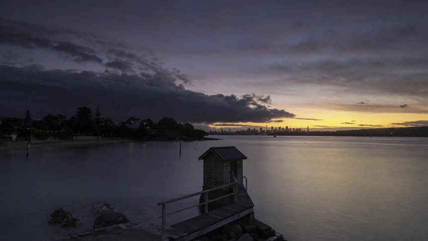 Clouds move across the sky over a coastal town located across the water from the city as night falls