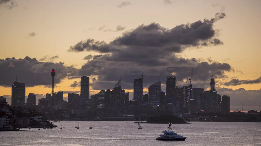 City skyline illuminated at dusk with tall buildings and partly cloudy sky over the water