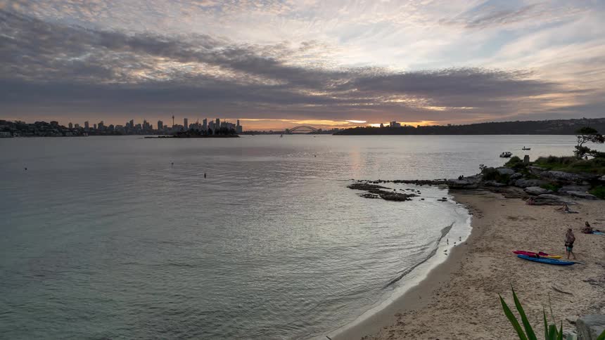 Beach with people in the water and on the sand at dusk under a cloudy sky