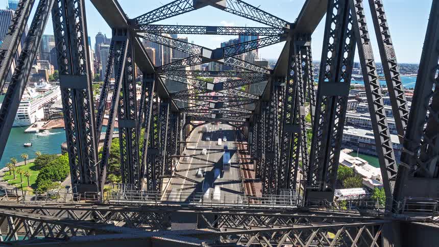Steel bridge structure with an urban roadway and buildings in the background under a clear sky