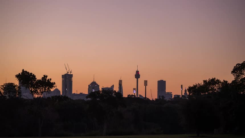 Construction cranes working on buildings at dusk as flood lights turn on