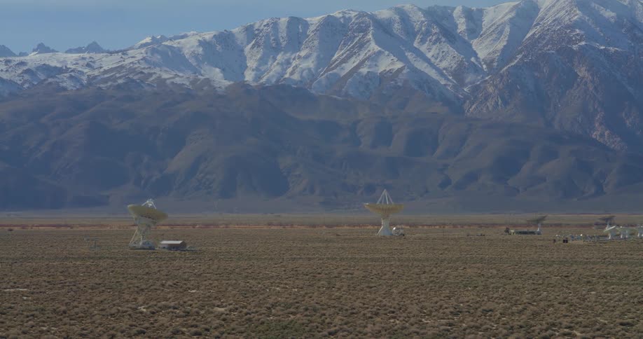 Snowy mountains tower over a plain containing satellite disks