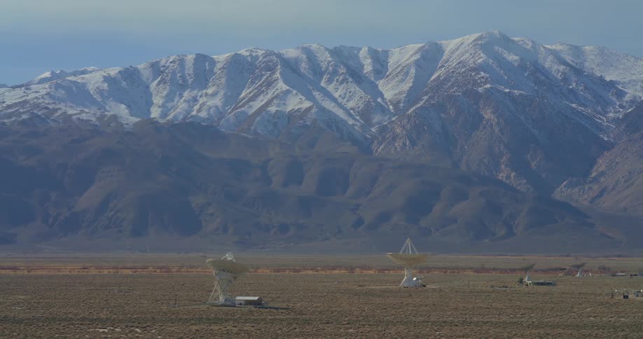 Satellite dishes on an arid plain with snowcovered mountains in the background