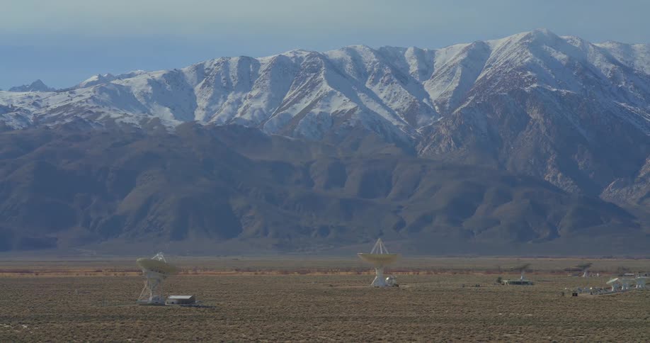 Satellite dishes in a desert area with snowcovered mountains in the background