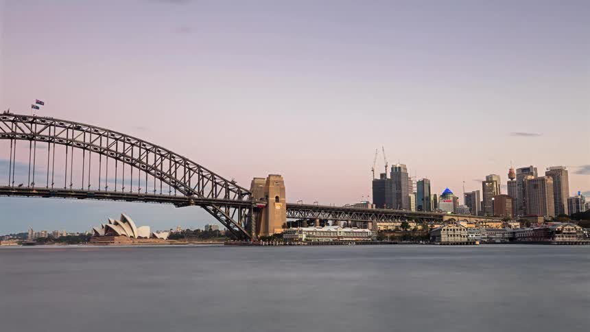 Watercraft move through the water passing under a bridge near sydney australia as night falls
