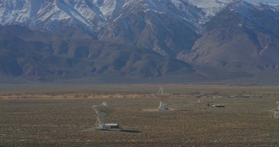 Radio telescopes stand in a field near the snowy mountains on a winter day