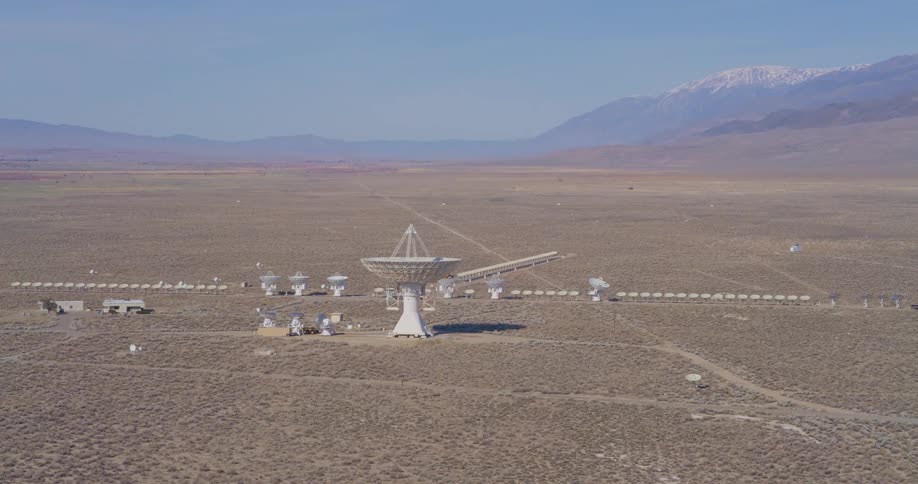 Array of satellite dishes spread across a desert plain with mountains in the background